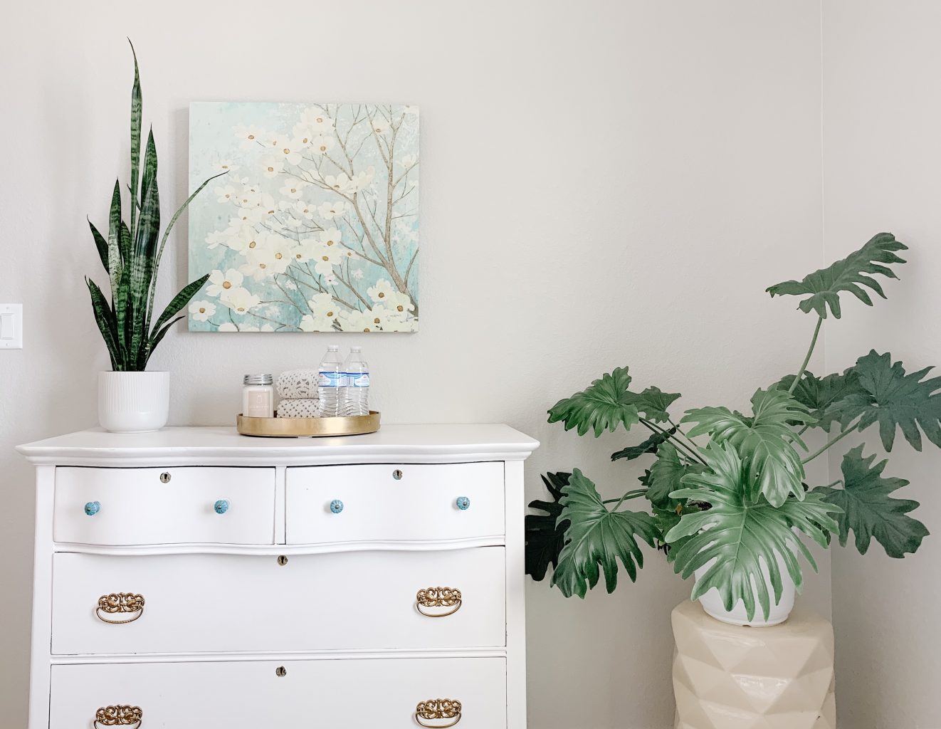 White dresser against wall with plants on it and next to it. 