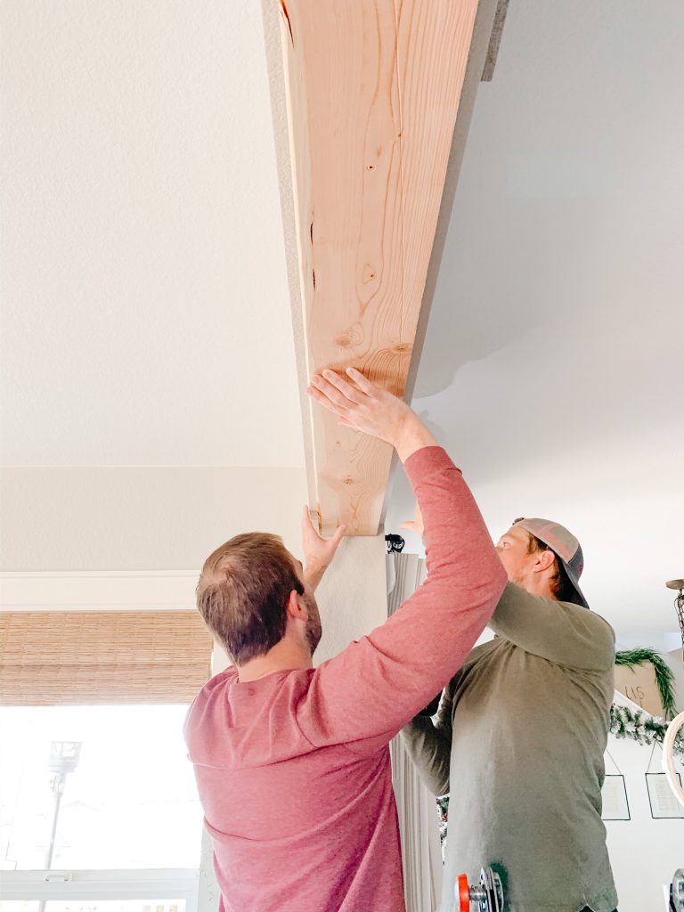 two men screwing in a piece of wood into a ceiling 