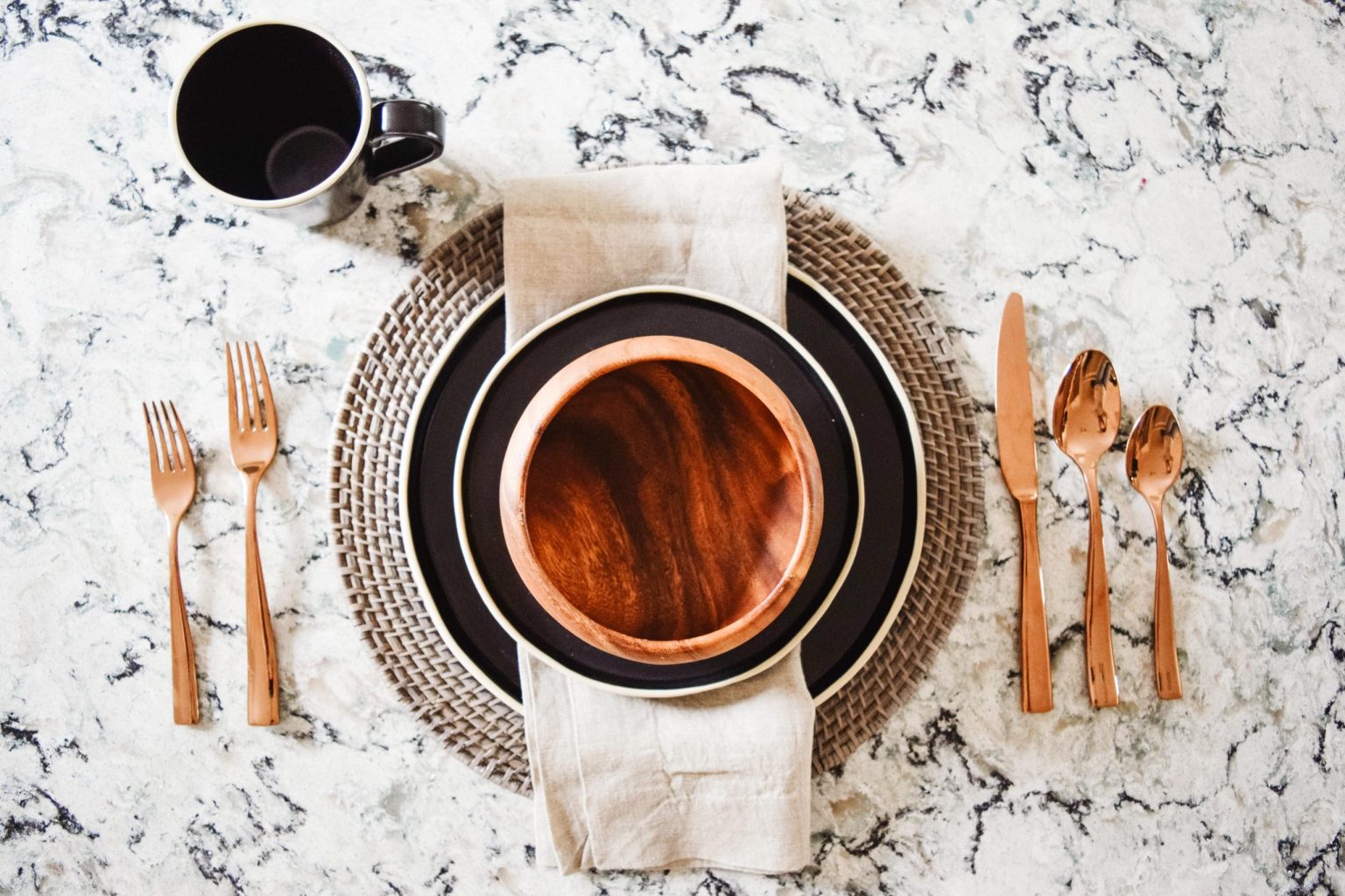 place setting with copper flatware and wood bowl on granite countertop