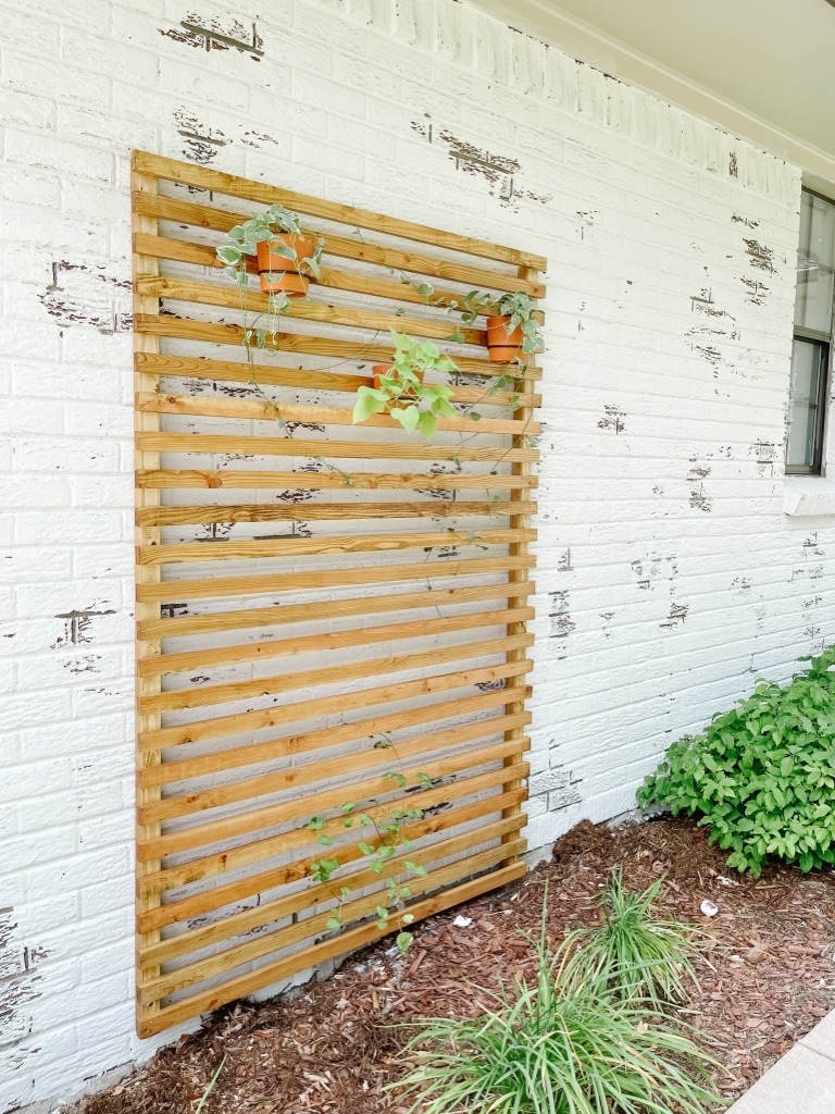 simple and affordable wood slat trellis against german schmear white brick with hanging planters and vinca vines