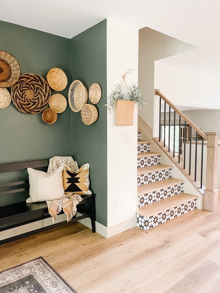 colorful peel and stick wallpaper at stair risers and dark green accent wall with black bench and wall baskets