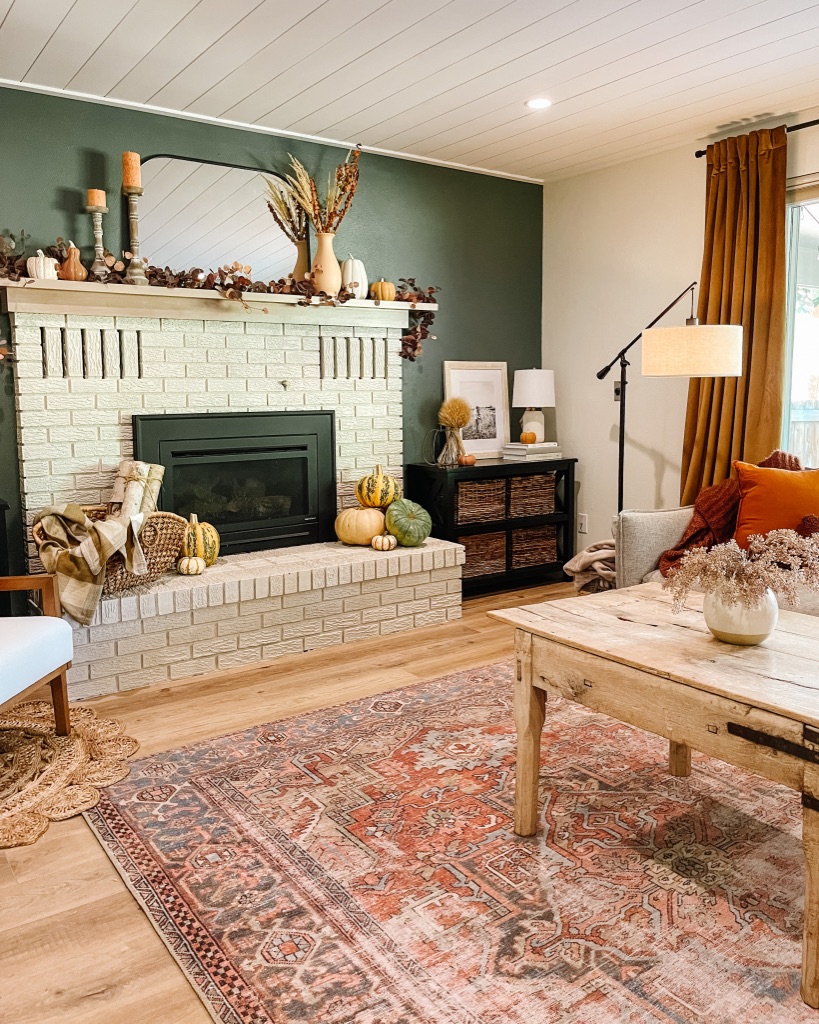 terracotta loloi rug in living room with cozy fall decor with moody dark green accent wall and white painted brick fireplace