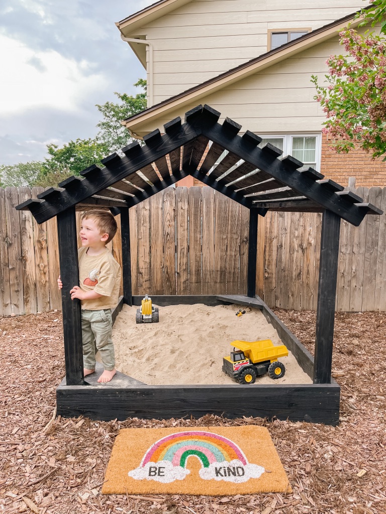 sandbox with house-like slatted wood roof and black wood stain