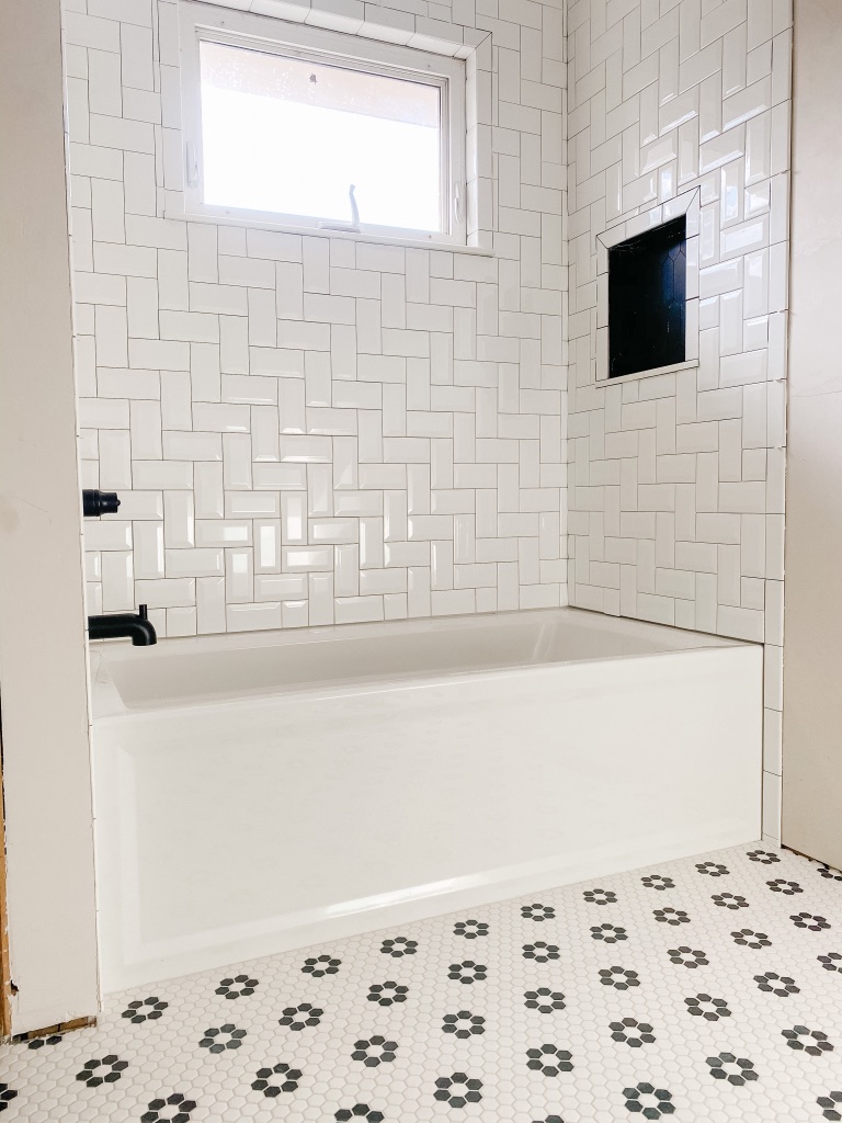 white 3 x 6 beveled subway tiles from Jeffry Court in a herringbone pattern at the shower wall with a black and white floral penny tile floor tile mosaic
