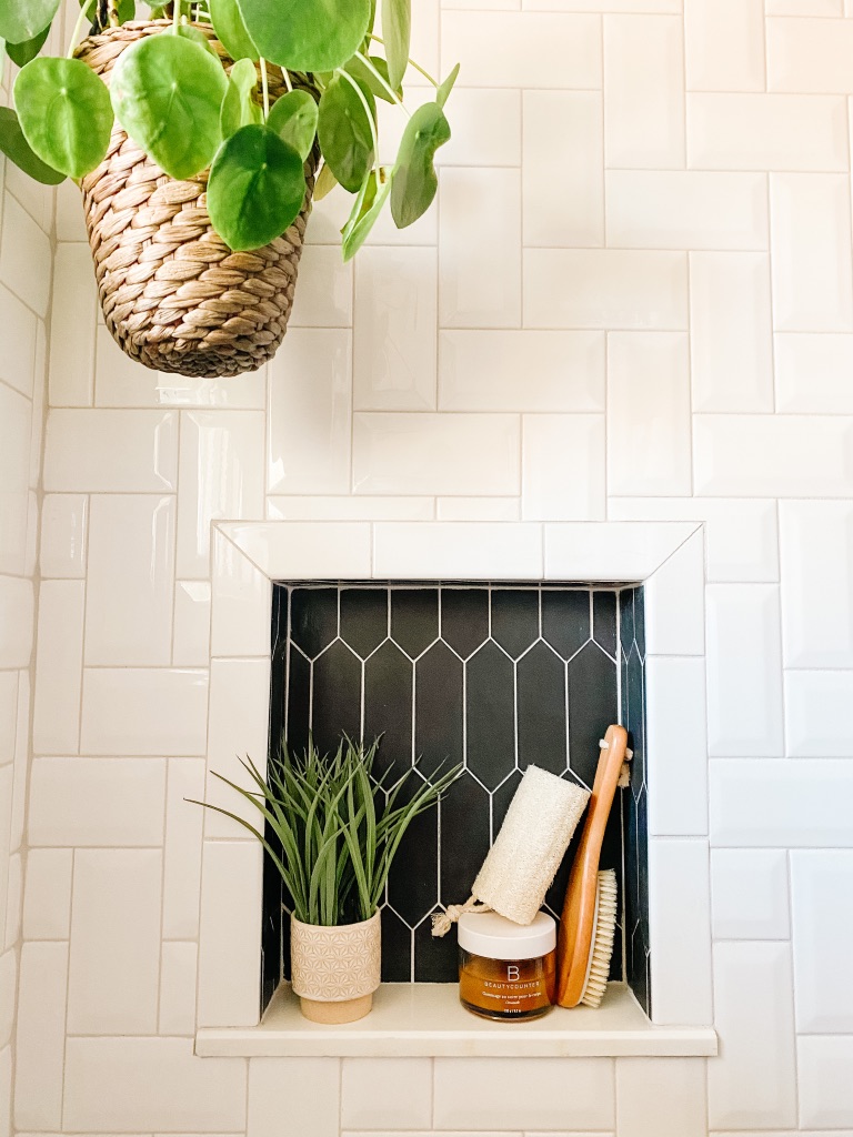 white subway tile in a herringbone pattern at shower wall with a black picket accent tile at the shower niche