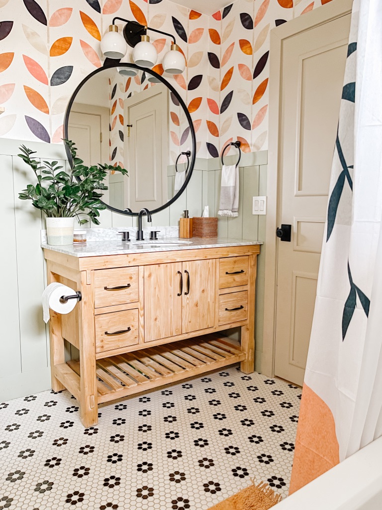 Colorful Boho 1970's Bathroom Remodel with natural wood vanity and oversized round mirror with black frame, colorful wallpaper and green shiplap