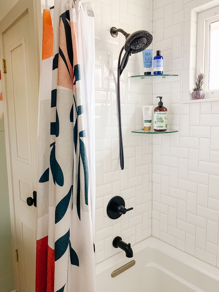 bathroom shower remodel with white bevel 3x6 subway tile in herringbone pattern and glass corner shower shelves, black Delta shower faucet and shower head