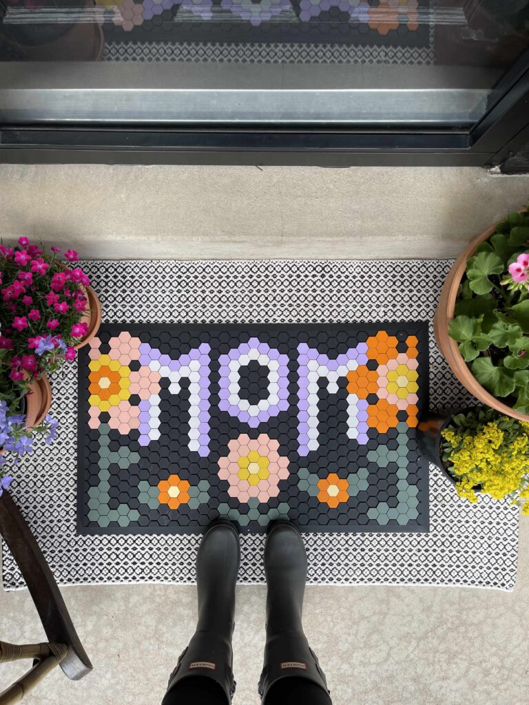 Letterfolk Tile Mat Mother's Day design with pink and orange flowers and lilac "mom" spelt out on standard size black tile mat at front porch with spring flowers